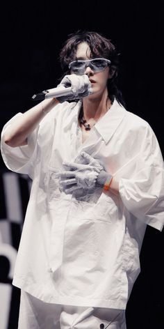 a man in white shirt and gloves holding a microphone to his ear while standing on stage