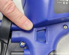 a finger is pressing the push button on a blue toy extruisher's seat