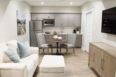 a living room and kitchen area with couches, chairs, table and television on the wall