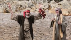 two men dressed in biblical garb standing next to each other with their hands up