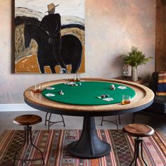 a poker table with two stools in front of it and a painting on the wall