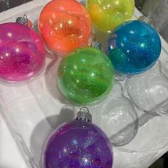 six glass ornaments in different colors on a white tray with silver trimming and glitter