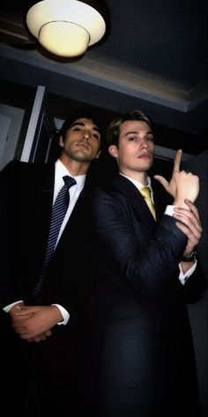 two men in suits standing next to each other and making the v sign with their fingers