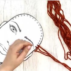 someone is drawing an elephant face on a piece of paper with red yarn next to it