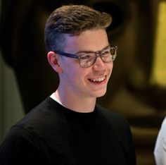 a young man wearing glasses smiles at the camera while standing in front of a statue