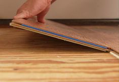 a person's hand on the edge of a wooden floor with a blue strip