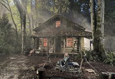 a woman sitting in front of a log cabin surrounded by trees and logs with the sun shining through the windows