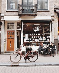 two people sitting at a table in front of a storefront with bikes parked on the sidewalk