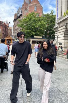 a man and woman walking down the street in front of some buildings with people on either side