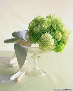 a vase filled with green flowers on top of a white table cloth covered tablecloth