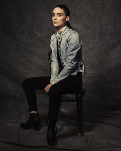 a woman sitting on top of a chair in front of a black background with her legs crossed