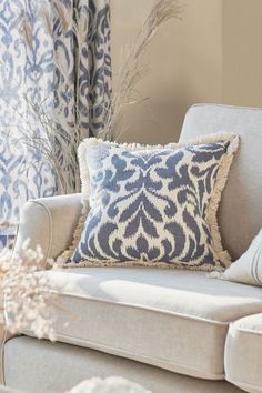 a blue and white pillow sitting on top of a couch next to a vase with flowers