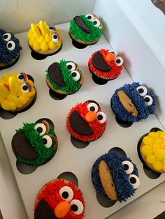 twelve decorated cupcakes in the shape of sesame street characters are displayed on a white box