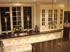 a kitchen with white cabinets and black counter tops, an island in the middle is surrounded by windows