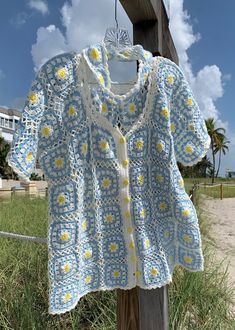 a blue and white crocheted sweater hanging on a wooden post in the grass