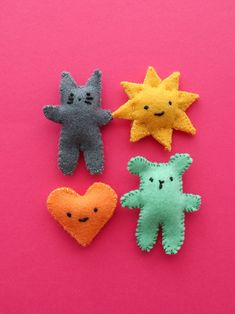 four felt toys are arranged on a pink surface, one is shaped like a star and the other has a smiling face