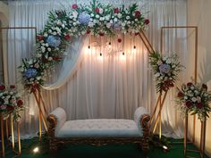 a decorated stage with flowers and greenery on the wall, along with two white couches