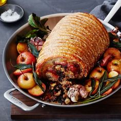 a large roasting pan filled with meat, apples and other food on top of a wooden cutting board