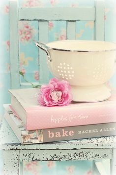 a white bowl sitting on top of a stack of books next to a pink flower