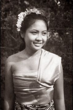 an old black and white photo of a woman in a dress with flowers in her hair