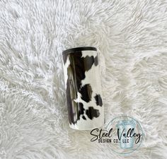 a black and white cow print tumbler sitting on top of a fluffy white rug