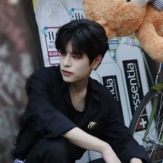 a young man sitting on the ground next to a teddy bear with his hands on his knees