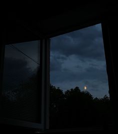 the moon is seen through an open window at night, with dark clouds in the background