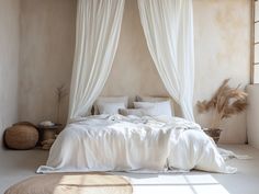 a bed with white sheets and pillows in a room next to a window that has sheer curtains on it