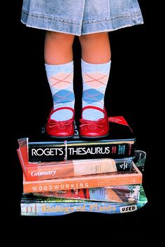 a doll standing on top of books with her legs crossed and red shoes in the air