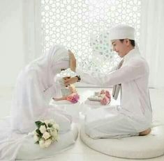 two people dressed in white sitting on bean bags and one is holding a small cake