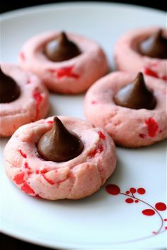 four pink cookies with chocolate on top and sprinkles in the middle sitting on a white plate