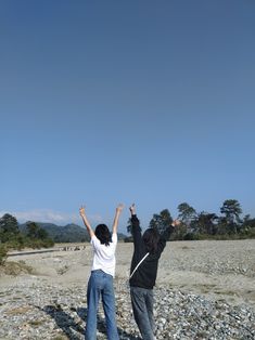 two women are flying a kite in the air on a rocky area with trees and mountains behind them