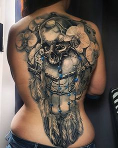 a woman's back with a skull and feathers tattoo on her stomach, which is adorned with blue beads