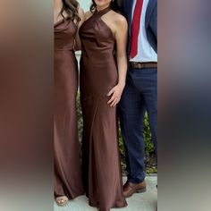 two women and a man standing next to each other in brown dresses with one woman wearing a red tie