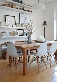 a dining room table with white chairs and bookshelves on the wall above it