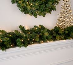 a christmas tree is sitting on top of a mantle next to a wreath with lights