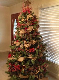 a christmas tree is decorated with gold and red ribbons, poinsettis and bows