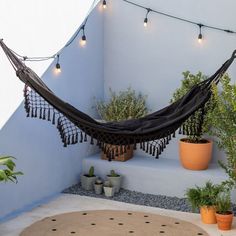 a hammock hanging from the side of a building next to potted plants