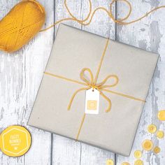 a present wrapped in gray paper with a yellow ribbon and tag next to it on a white wooden surface