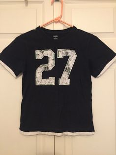 Gymboree Boys Navy Blue Sports Number 27 Layered Look T-shirt Jersey Sz 7 EUC. Condition is "Pre-owned". Shipped with USPS First Class. Navy blue with distressed white screen printed number 27. Decorative green stitching outlines the numbers. Shirt has a layered distressed look around the edges. Preowned in excellent condition. Minimal wash wear. Blue Crew Neck T-shirt With Number Print, Casual Sports T-shirt With Number Print, Casual Blue Tops With Number Print, Cotton Tops With Number Print For Sports Season, Navy Blue Graphic Tee, Sports Numbers, Number 27, Number Shirt, White Screen