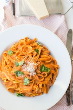 a white plate topped with pasta covered in sauce and parmesan cheese next to silverware