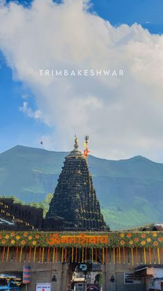 an ornate temple with mountains in the background and blue sky above it that says trimbakeshwar