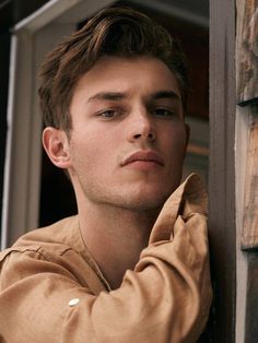 a young man leaning against a wooden wall with his hand on the side of him