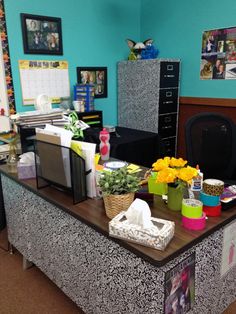 an office desk with many items on it and flowers in vases next to the table