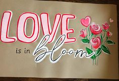 a piece of paper with the words love is in bloom painted on it and flowers