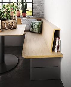 a corner table with some plants and books on it in front of a large window