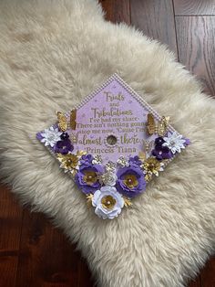 a purple and white graduation cap on top of a furry pillow with flowers around it