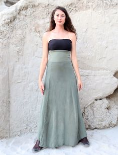 a woman standing in front of a stone wall wearing a green skirt and black top