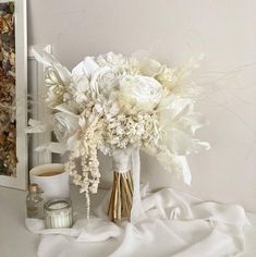 a bouquet of white flowers sitting on top of a table next to a cup and candle