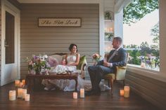 a bride and groom sitting on a couch in front of a window with lit candles